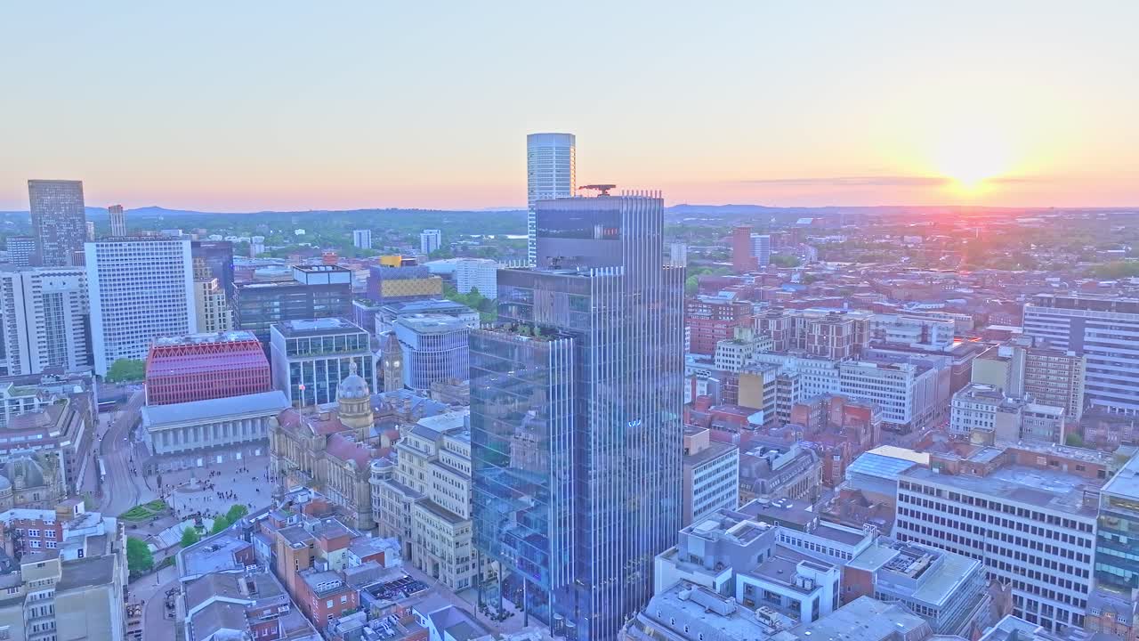 erial footage shows a slow drone ascent above Pigeon Park in Birmingham, featuring the city’s tallest buildings, including 103 Colmore Row and Town Hall, under a glowing sunset