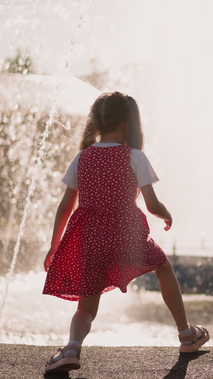 Playful little children with mother have fun near fountain water on city square backside view. Woman takes care of active kids outdoors. Urban summer