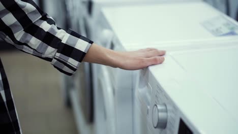 choosing washing machine in appliance store. running hand by the row. unrecognizable woman in household appliances department