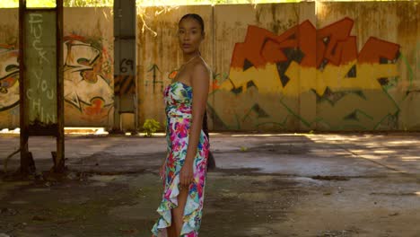 sexy caribbean girl in a long flowing dress walks toward grafitti on the wall before turning around