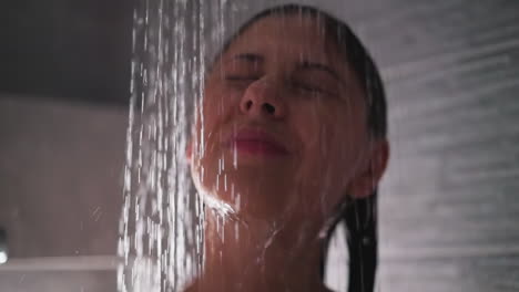 mujer se encuentra debajo de verter agua en la ducha de cerca. dama soñadora con los ojos cerrados lava el cuerpo con procedimientos de spa en el baño. cuidado de la belleza