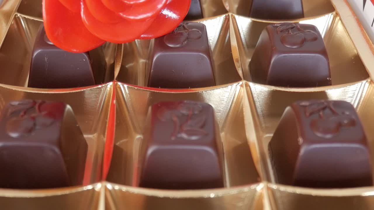 Red rose placed next to chocolate truffles in a golden box for Valentine's Day