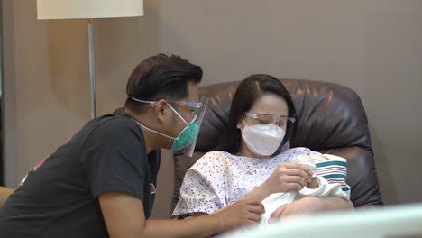 parents with face mask talking to each other while the mother is holding the baby