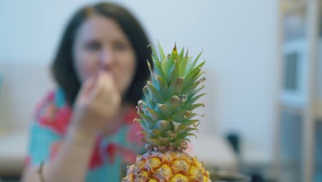 piña en un plato rojo contra una dama borrosa comiendo frutas