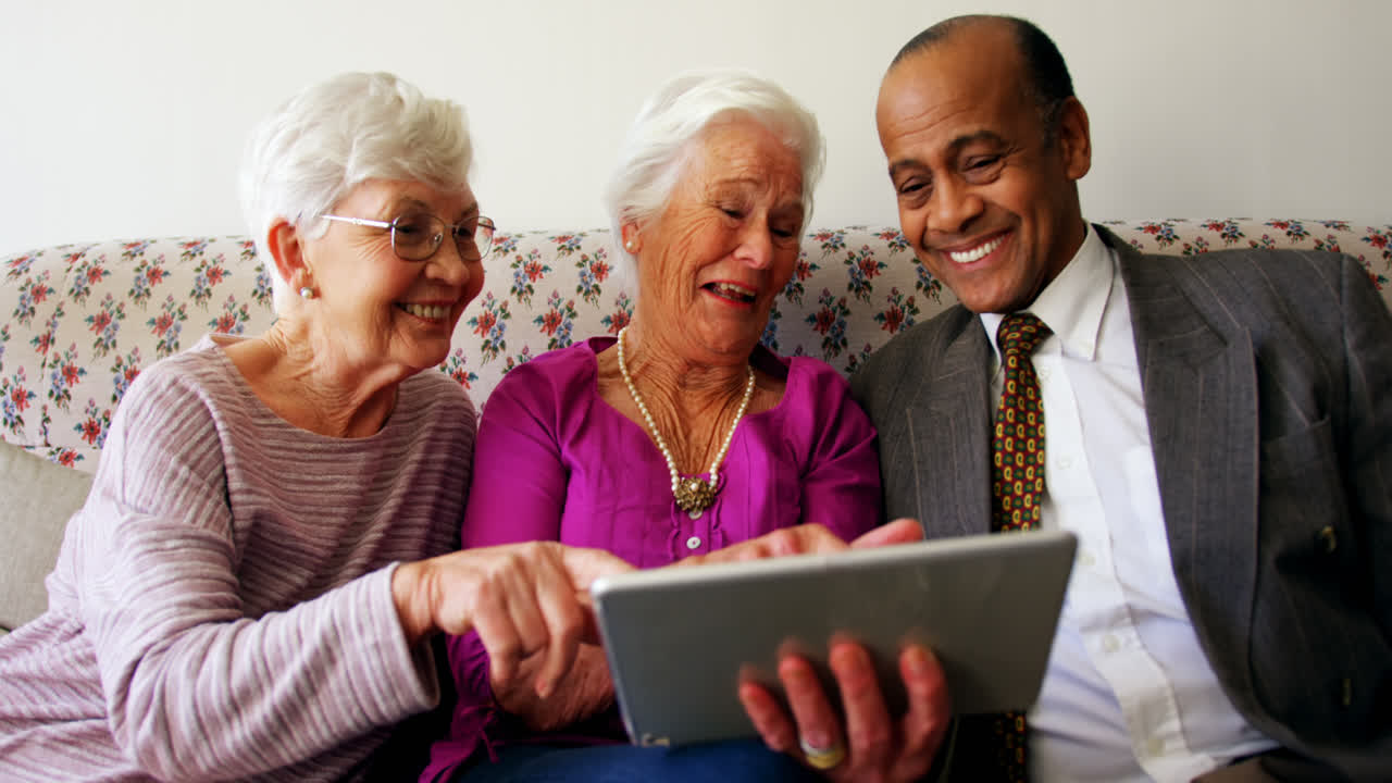 Group of active mixed-race senior friends discussing over digital tablet in nursing home 4k