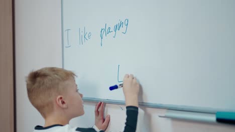 little boy near the blackboard. schoolboy standing near the white board and writing sentences with a marker. elementary school. back to school.