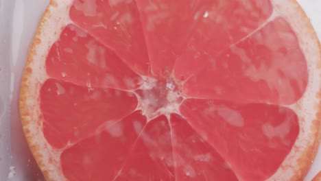 Video-of-water-drops-falling-onto-slice-of-red-grapefruit-with-copy-space-on-white-background