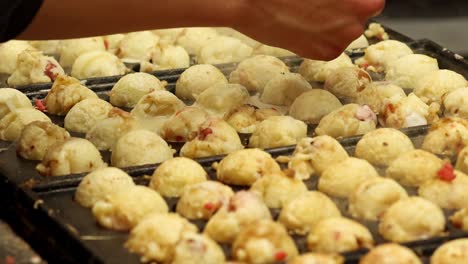 close-up of hands using skewers to turn takoyaki balls on a hot grill.