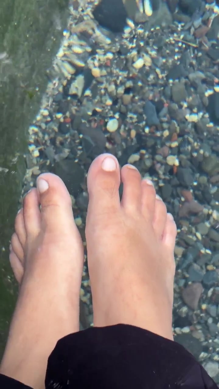 Person Relaxing Feet in Clear Shallow Water Over Pebbles