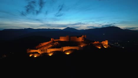 imágenes aéreas de un castillo iluminado en la cima de la colina al anochecer