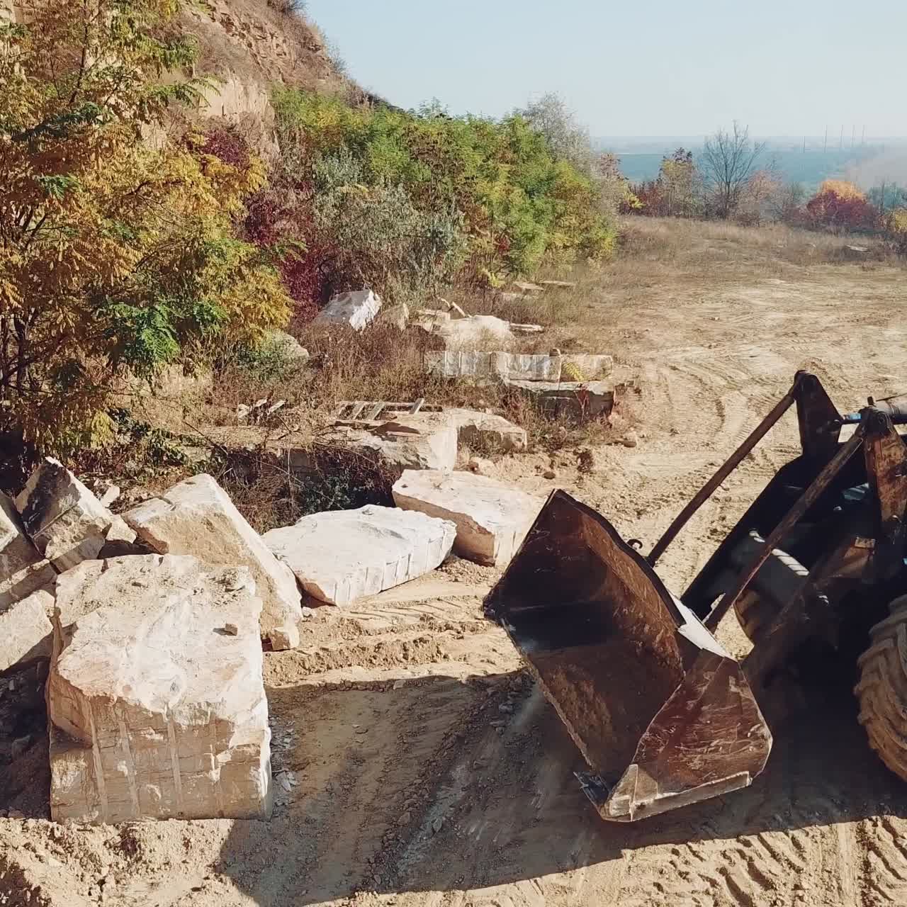 professional bulldozer with a bucket is picking up stones on sandy quarry against the backdrop of wild nature. Close-up