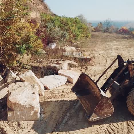 professional bulldozer with a bucket is picking up stones on sandy quarry against the backdrop of wild nature. close-up