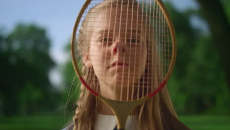 cute smiling girl look camera through racket net closeup. kid make funny face