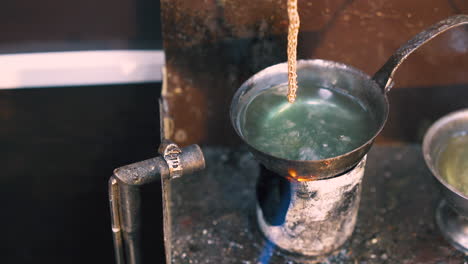 jeweler puts chain into boiling liquid on table closeup