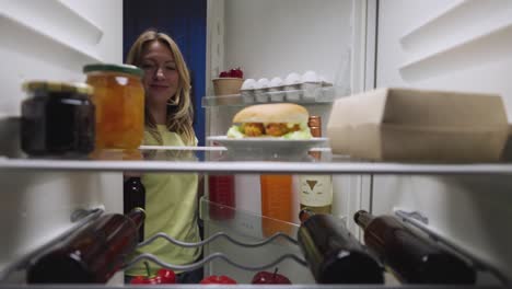 woman reaching into refrigerator at night