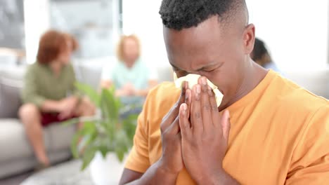 hombre emocional llorando con diversos amigos hablando en segundo plano durante una sesión de terapia de grupo