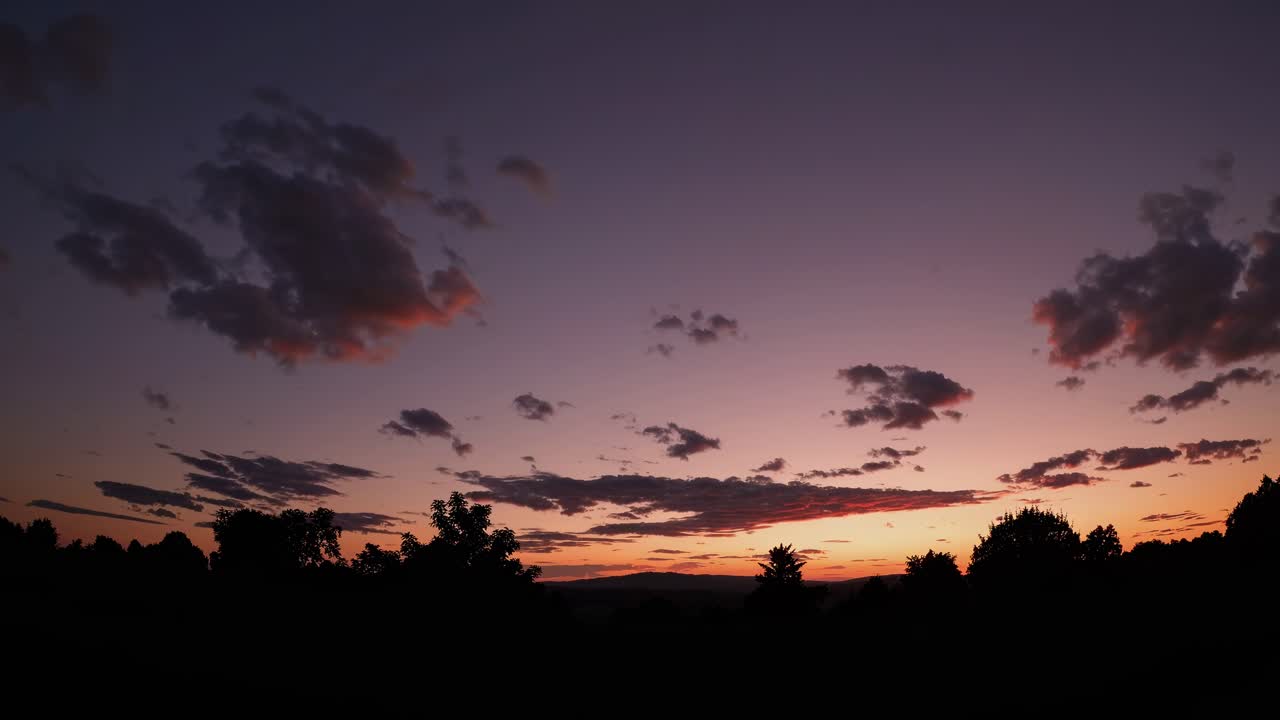 Ein Weitwinkel-Video fängt eine ruhige Sonnenuntergangslandschaft mit Baum силуetten vor einem Dämmerungshimmel ein