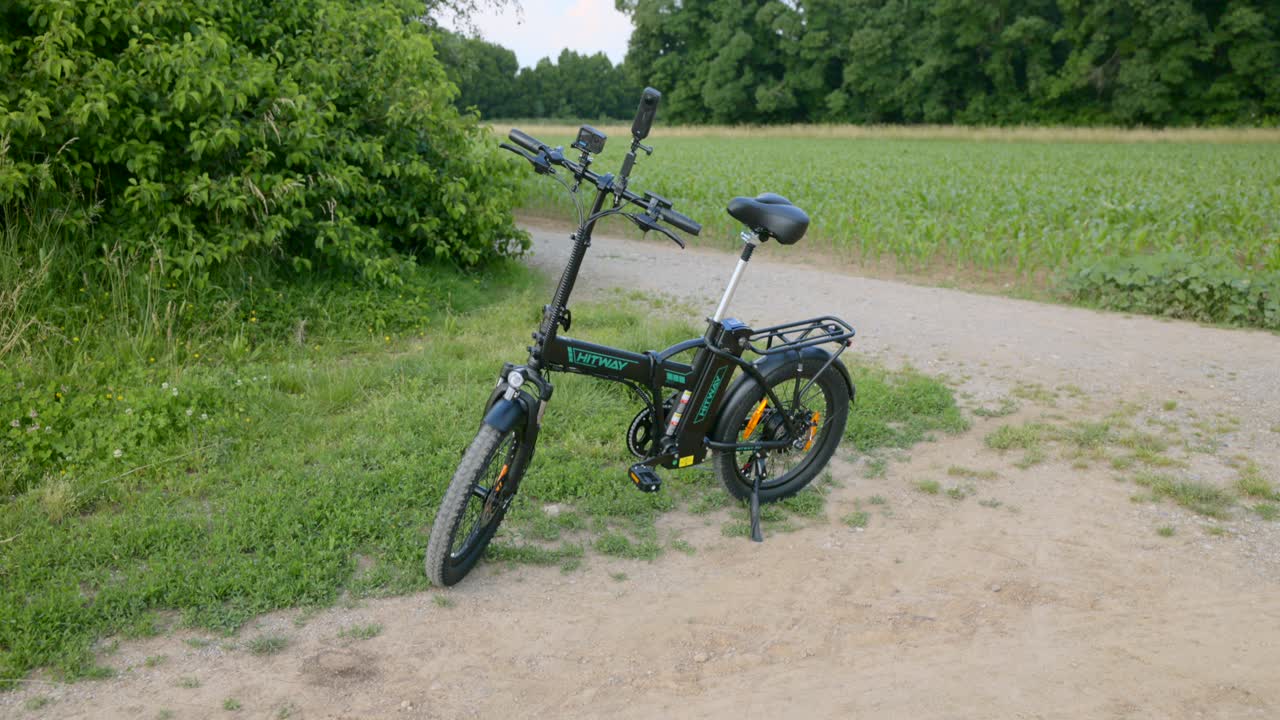 Electric folding bike parked on a countryside dirt path surrounded by greenery and farmland, captured during a calm summer day. Perfect for eco-friendly transport