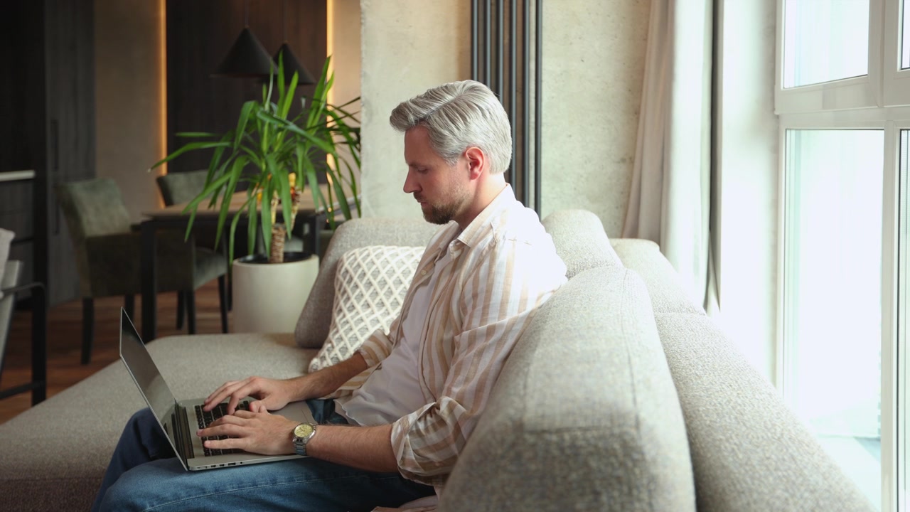 Focused Man Typing on Laptop While Sitting on Sofa at Home