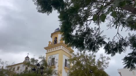 Revealing-view-of-the-church-tower-in-Spain,-rises-majestically-against-the-backdrop-of-a-moody-and-cloudy-sky-during-windy-day