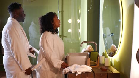 side view happy loving african american husband and pregnant wife dancing looking at mirror in bathroom smiling kissing. cheerful couple having fun in the morning at home indoors.