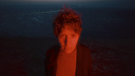 portrait of woman illuminated by red light near dark frozen lake at night