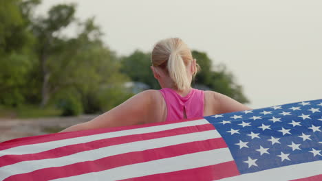 woman in sportswear with usa flag on her shoulders walks along the seashore