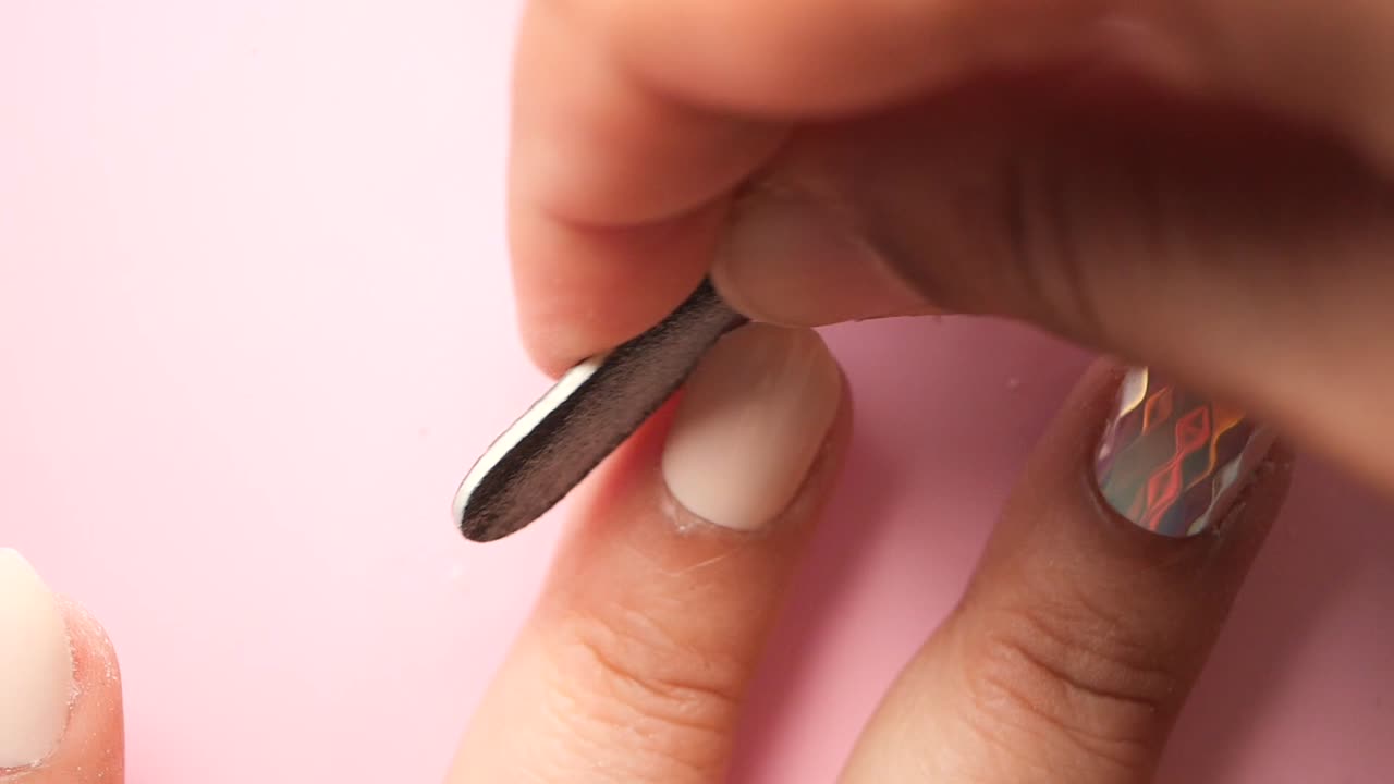 Nail art process: Filing and shaping beige nails with holographic design