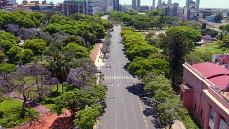 dolly in aerial view of a wide and lonely avenue on a sunny day in buenos aires, cyclist and car crossing each other