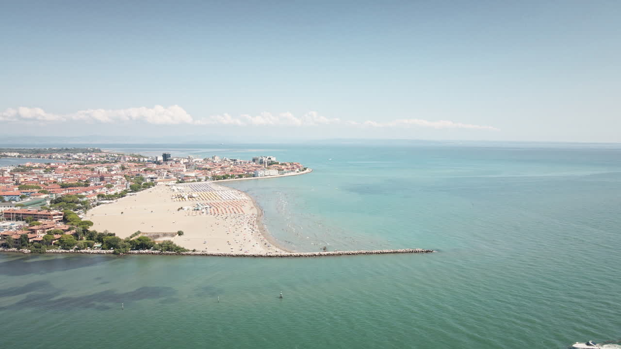 Drone 4K UHD si allontana fluidamente dalla spiaggia sabbiosa di Grado, rivelando un molo in pietra e il vasto Mare Adriatico—ideale per film di viaggio e inquadrature di apertura.