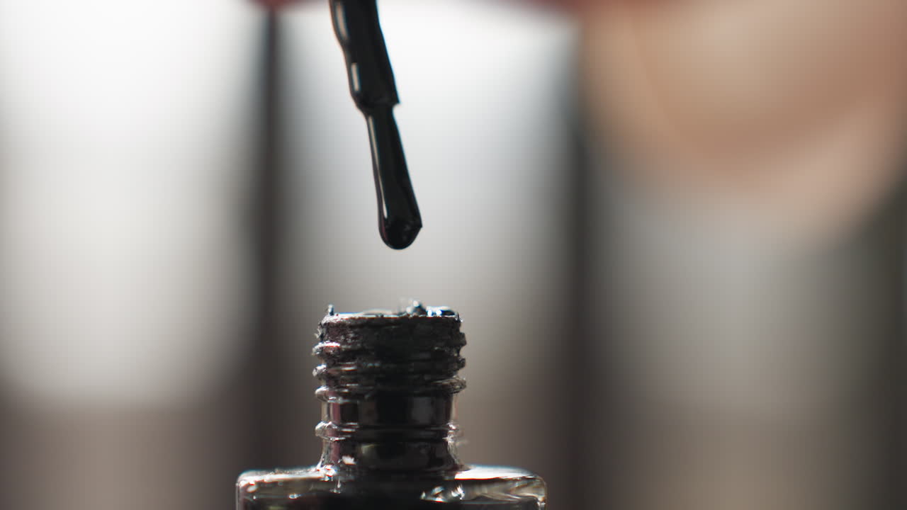 Close up smooth female hands twist cap of nail varnish bottle, rolling lid before removing, soft light indoors highlights skin texture and glossy container during beauty routine on tabletop