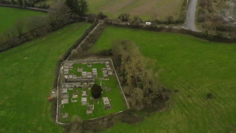 Panoramic-aerial-overview-above-graveyard-off-secluded-countryside-road-in-green-pastures