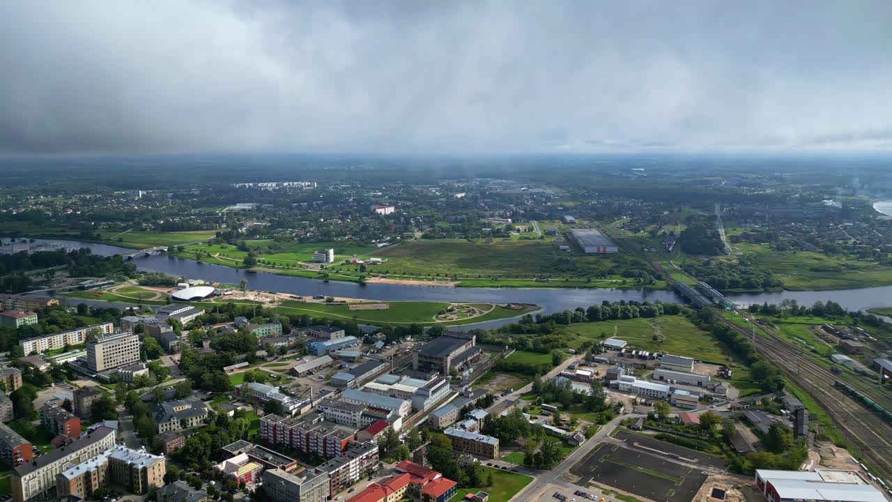 Aerial view of a green city with a river and a bridge on a cloudy day with sun rays, going left