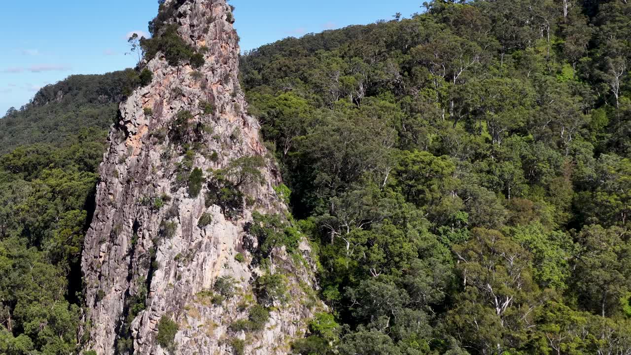 Aerial footage captures the rugged Nimbin Rocks against lush greenery under clear blue skies in Nimbin, NSW, Australia