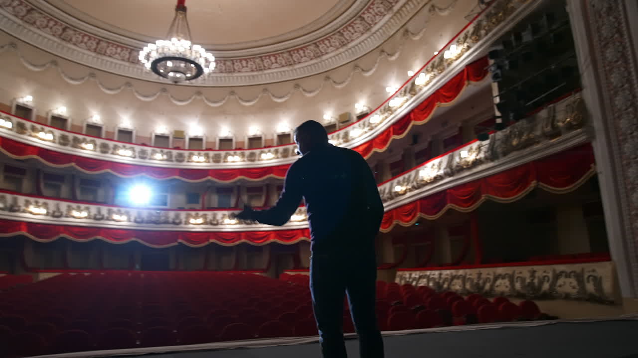 Man on stage on classical theater hall background. Rehearsal before the performance. Actor is talking to the empty auditorium. View from scene.