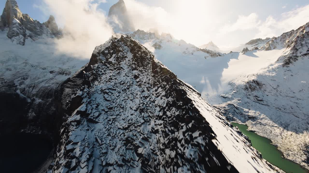 Cinematic aerial FPV drone shot gliding over snowy Mount Fitz Roy peaks in Patagonia, Chile. Argentina. Sunlit summits, scattered clouds, and stunning alpine landscape, flying toward low golden sun.