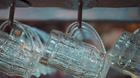 old fashioned glass mugs hang on rack over counter in pub