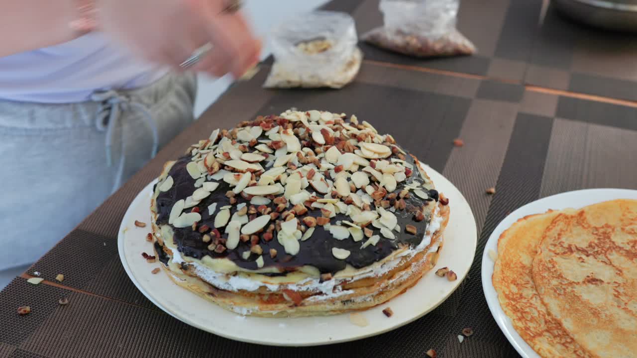 Krep pastasının üzerine dilimlenmiş badem ve fındık serpen eller. Yakın çekim