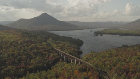 pushing in on a railroad trestle leading towards a distant mountain in an early fall forest aerial