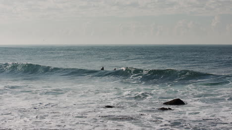 Three-surfers-sit-in-the-line-up-waiting-for-a-perfect-wave-in-the-dark-blue-pacific-ocean-water