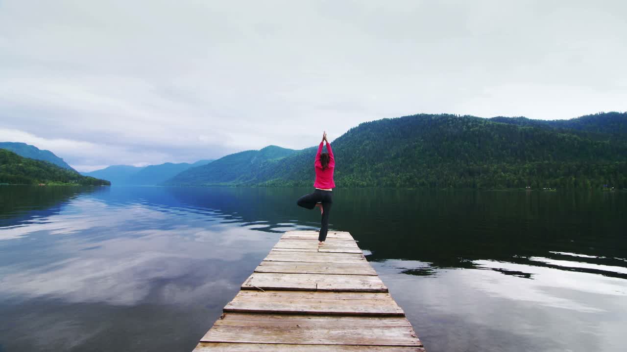 Donna che pratica yoga su un pontile di legno in riva a un lago