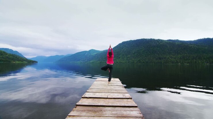 Donna che pratica yoga su un pontile di legno in riva a un lago