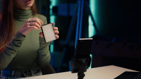gen z chica en el estudio revisando mini luces rgb, usando teléfono móvil para grabar