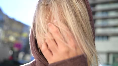 close up portrait of a young blonde female wearing a hoodie in the city centre in early morning sunshine with the sun flaring the lens