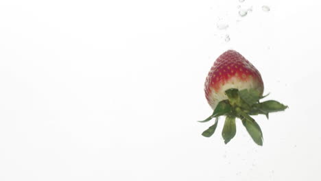 a slow motion of a strawberry being dropped in a clear water