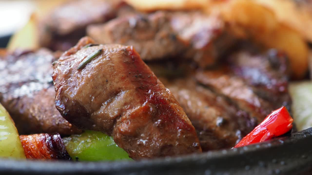 Detalhe de carne grelhada e vegetais em uma frigideira quente.