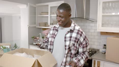 Feliz-Hombre-Afroamericano-Desempacando-Cajas-En-La-Cocina-De-Casa,-Cámara-Lenta