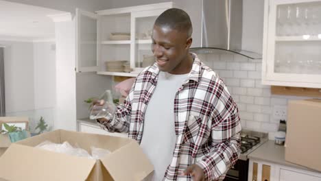 feliz hombre afroamericano desempaquetando cajas en la cocina en casa, cámara lenta