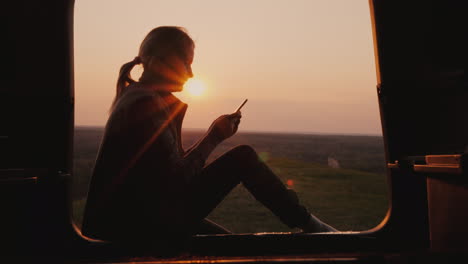 A-Woman-Uses-A-Smartphone-In-The-Trunk-Of-A-Car-In-Touch-While-Traveling