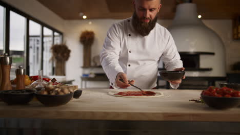 professional cook making pizza in culinary kitchen. chef man spreading ketchup.